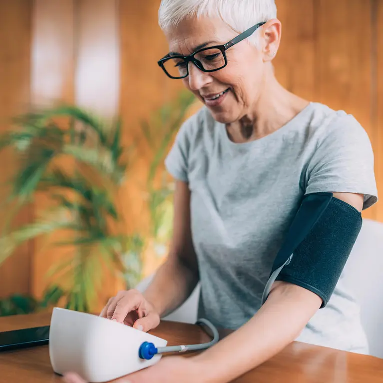 Man sieht eine Frau, die ihren Blutdruck mit einem Blutdruckmessgerät prüft.