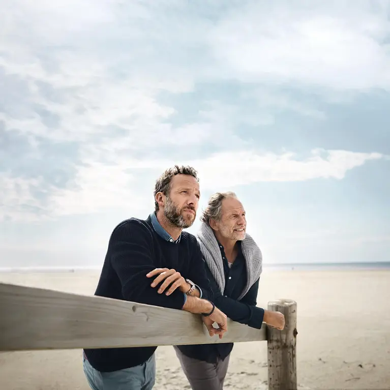 Zwei Männer stehen am Strand und schauen in die Ferne.